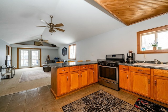 kitchen featuring a peninsula, lofted ceiling, stainless steel gas range, dark countertops, and open floor plan