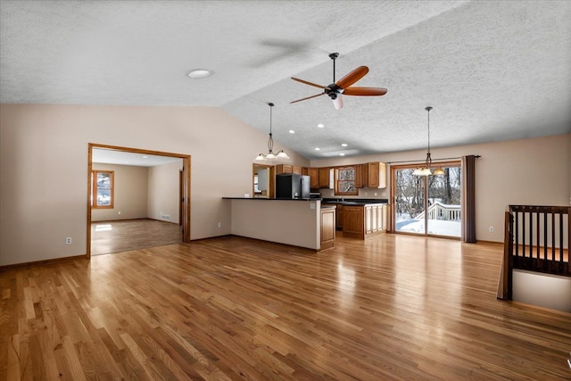 unfurnished living room featuring lofted ceiling, light wood finished floors, a wealth of natural light, and ceiling fan with notable chandelier