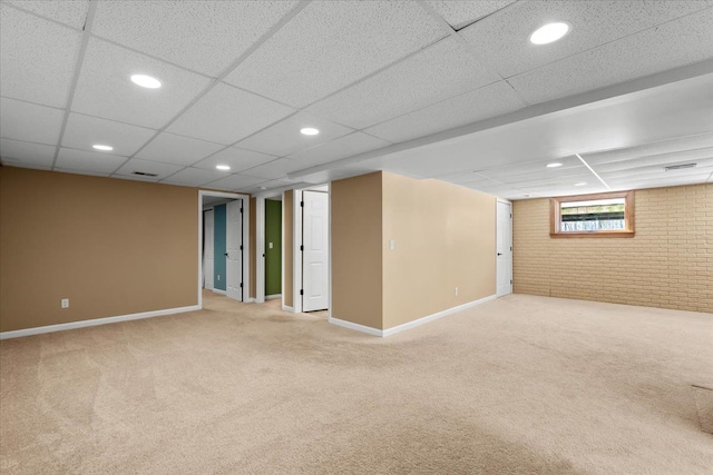 basement with light carpet, baseboards, brick wall, a paneled ceiling, and recessed lighting