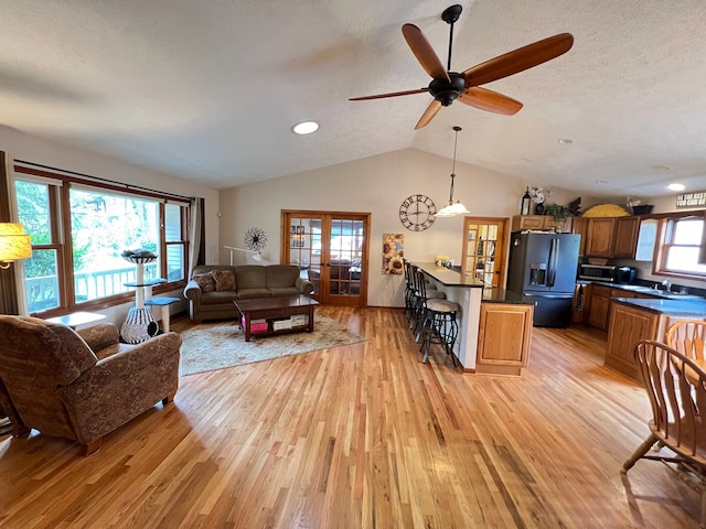 living room featuring vaulted ceiling, french doors, a textured ceiling, and light wood-style floors