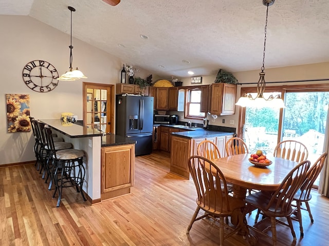 dining space featuring vaulted ceiling, a textured ceiling, light wood-style flooring, and baseboards