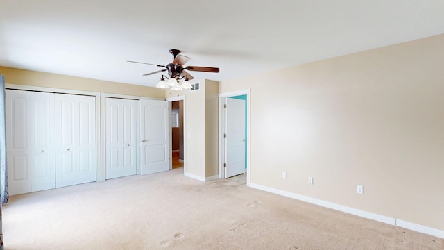 unfurnished bedroom with baseboards, visible vents, two closets, ceiling fan, and light carpet