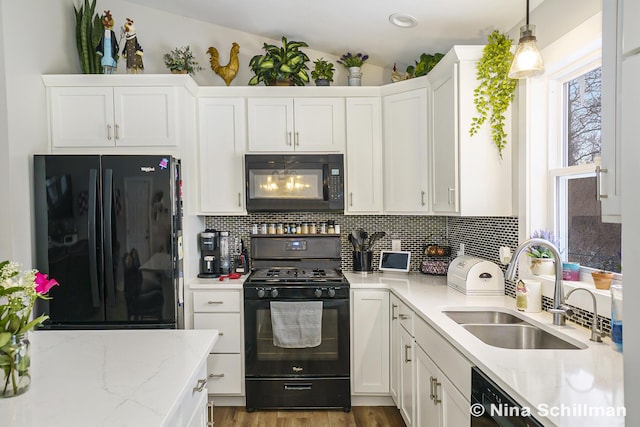 kitchen with pendant lighting, tasteful backsplash, black appliances, white cabinets, and a sink