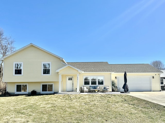 tri-level home with a front yard, a shingled roof, concrete driveway, a garage, and outdoor lounge area