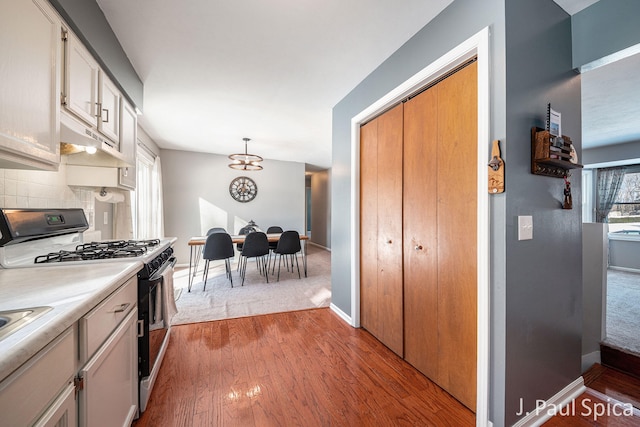 kitchen featuring light countertops, light wood-style flooring, black gas stove, white cabinetry, and hanging light fixtures