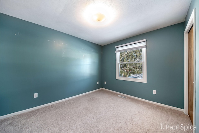 carpeted empty room featuring baseboards, a textured ceiling, and visible vents