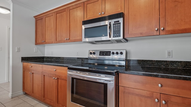 kitchen with light tile patterned floors, appliances with stainless steel finishes, brown cabinetry, ornamental molding, and dark stone counters