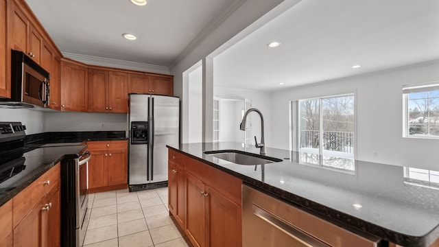 kitchen with stainless steel appliances, a sink, brown cabinetry, an island with sink, and dark stone countertops