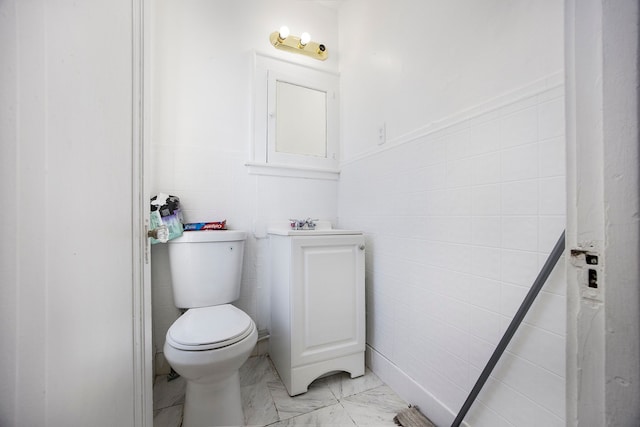 bathroom featuring marble finish floor, wainscoting, toilet, and tile walls