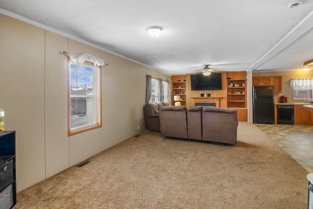 living area featuring built in shelves, a fireplace, light colored carpet, visible vents, and ceiling fan