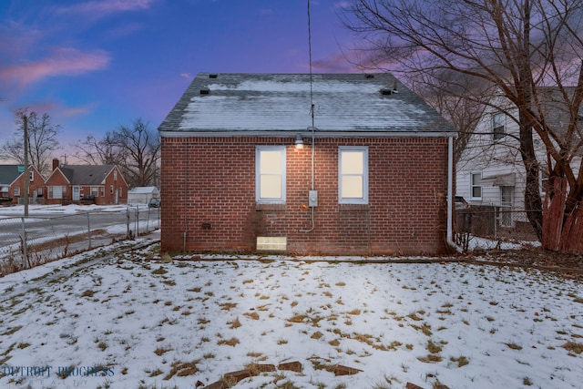 view of snowy exterior featuring roof with shingles, fence, and brick siding