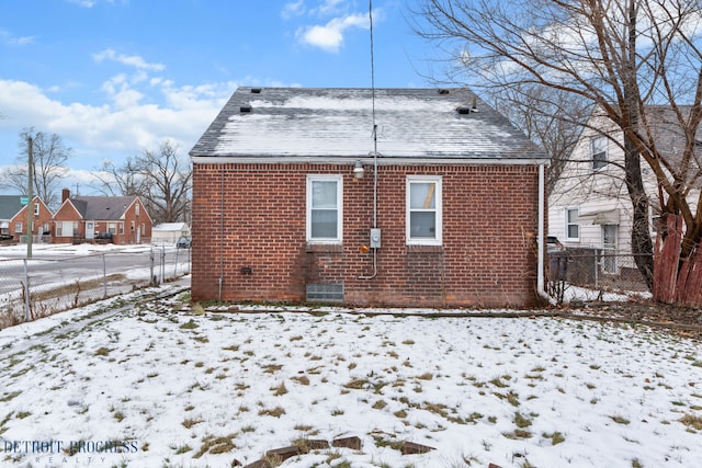 snow covered property with brick siding, fence, and roof with shingles