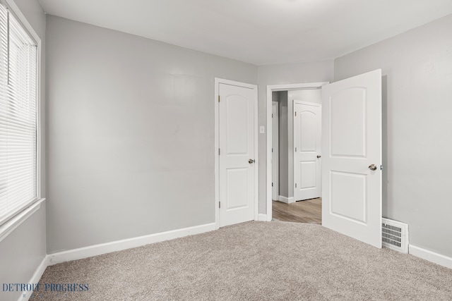 unfurnished bedroom with light carpet, baseboards, multiple windows, and visible vents