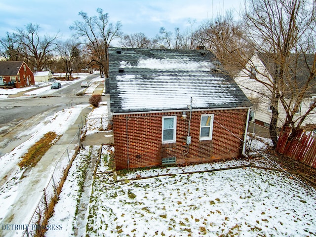 view of snow covered exterior with brick siding and roof with shingles