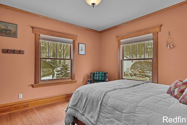 bedroom with baseboards, multiple windows, wood finished floors, and ornamental molding