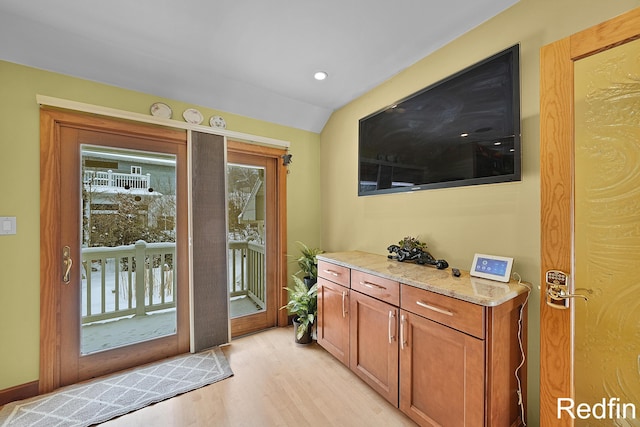 doorway to outside with light wood finished floors and vaulted ceiling