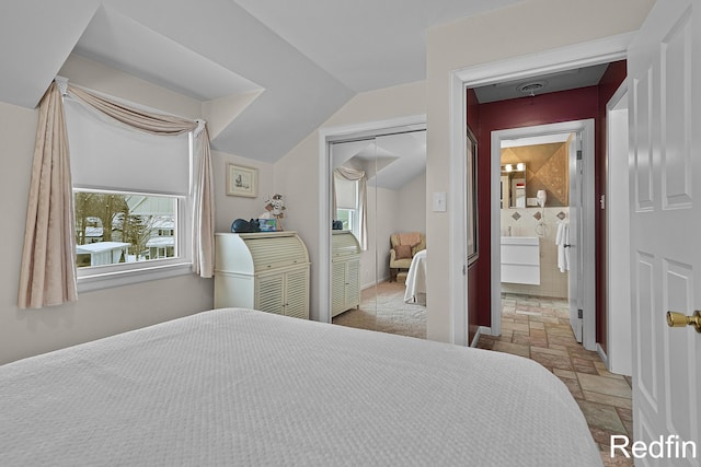 bedroom with stone tile flooring, ensuite bath, a closet, and lofted ceiling