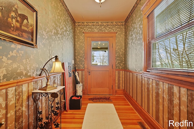 doorway to outside featuring wallpapered walls, visible vents, light wood finished floors, and a wainscoted wall