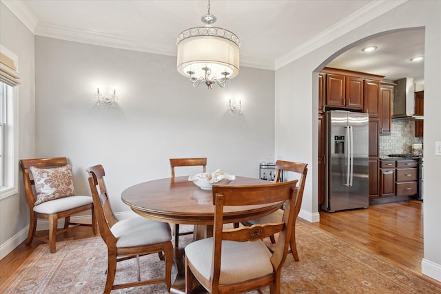 dining area featuring arched walkways, baseboards, light wood-style floors, and ornamental molding