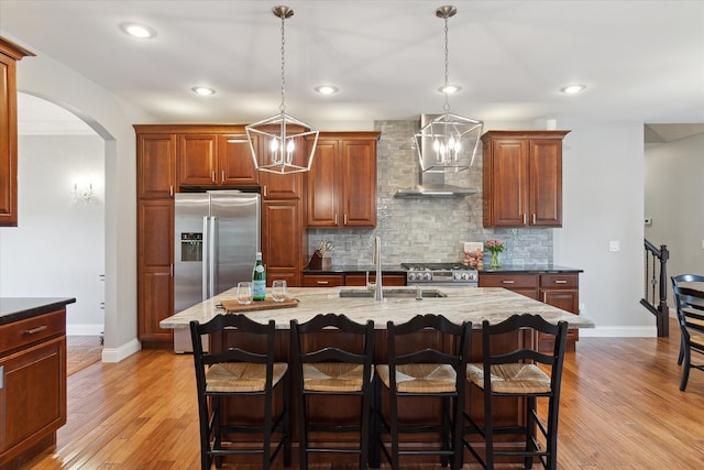 kitchen with a breakfast bar, a sink, stainless steel appliances, wall chimney range hood, and decorative backsplash