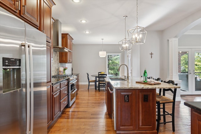 kitchen with a kitchen bar, a sink, stainless steel appliances, french doors, and wall chimney exhaust hood