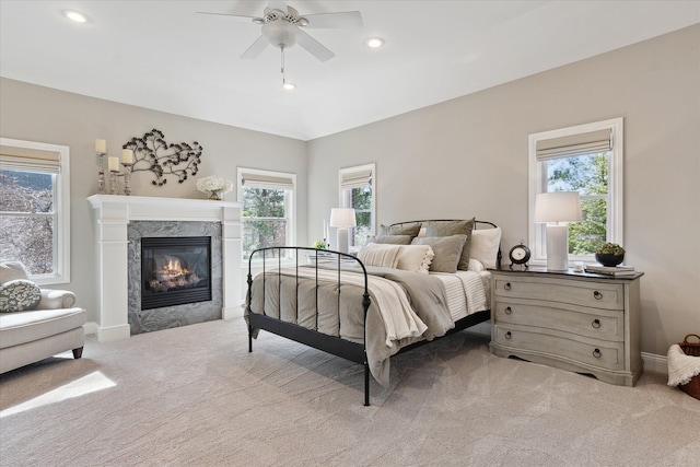 bedroom featuring light colored carpet, baseboards, a high end fireplace, and ceiling fan