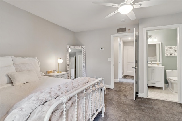 bedroom featuring visible vents, ceiling fan, baseboards, ensuite bathroom, and dark colored carpet