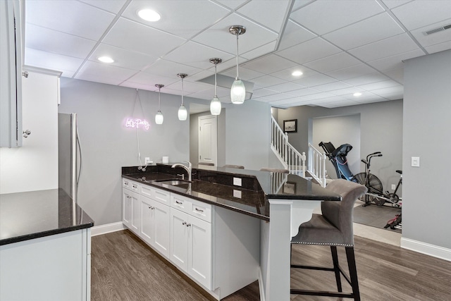 kitchen featuring visible vents, a peninsula, a kitchen breakfast bar, white cabinetry, and a sink