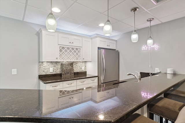 kitchen featuring a kitchen bar, dark stone countertops, tasteful backsplash, white cabinetry, and freestanding refrigerator