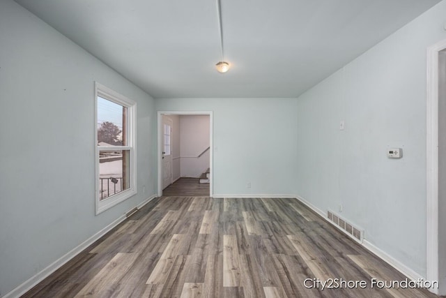 unfurnished room featuring baseboards, visible vents, and wood finished floors