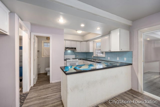 kitchen featuring a sink, a peninsula, dark countertops, and white cabinets