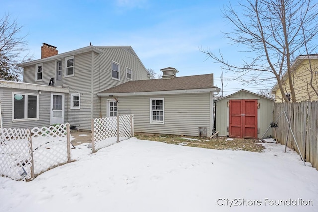 snow covered rear of property featuring a chimney, a shed, an outdoor structure, and fence private yard