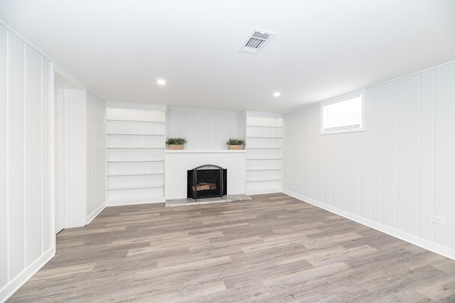 basement with a brick fireplace, visible vents, built in shelves, and light wood-type flooring