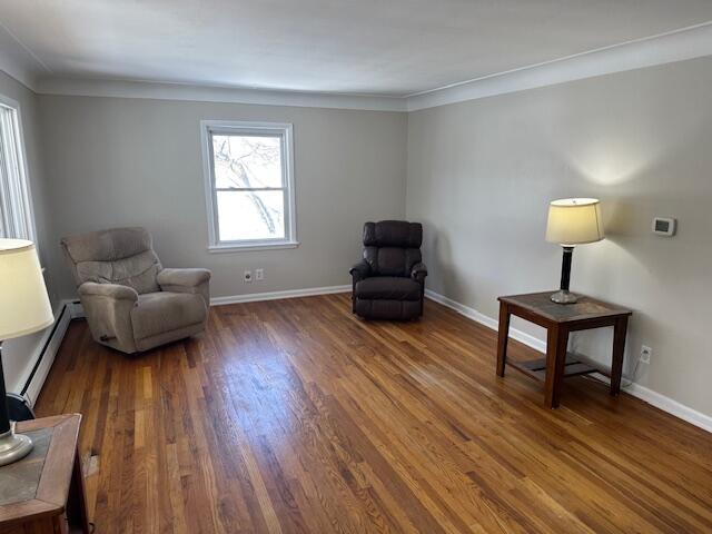 living area featuring baseboards, baseboard heating, crown molding, and dark wood-type flooring