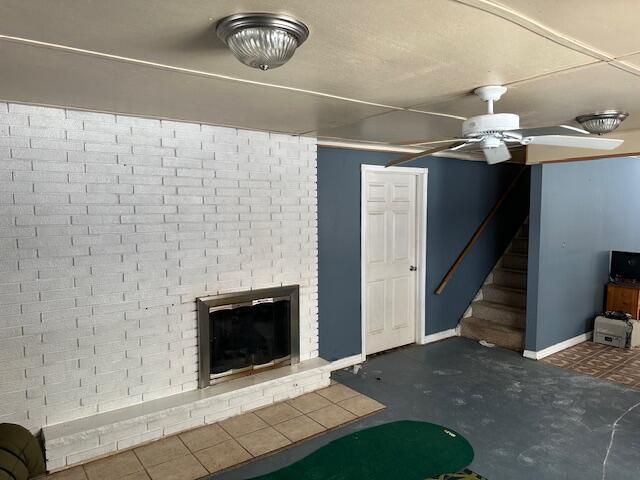 unfurnished living room with stairway, baseboards, a ceiling fan, and a brick fireplace