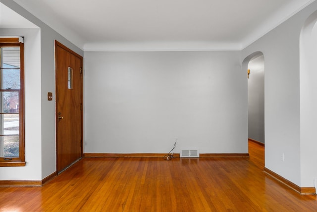 spare room featuring baseboards, visible vents, arched walkways, and wood finished floors