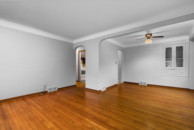 empty room with arched walkways, wood finished floors, and visible vents