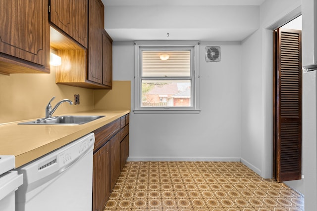 kitchen featuring light floors, light countertops, a sink, dishwasher, and baseboards