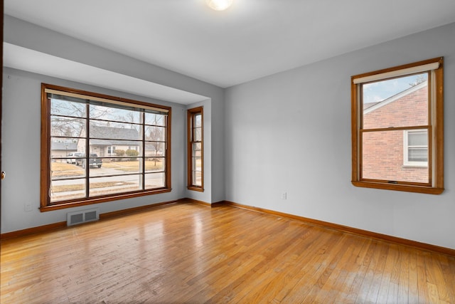 empty room with light wood-style floors, baseboards, visible vents, and a wealth of natural light