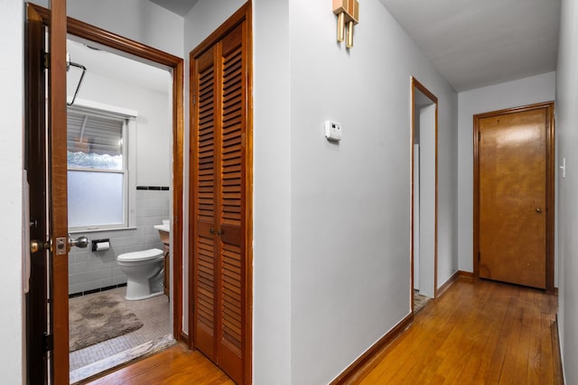 hall featuring a wainscoted wall, light wood-type flooring, and tile walls