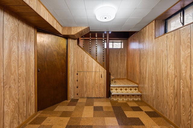 below grade area featuring wood walls, baseboards, stairway, and tile patterned floors