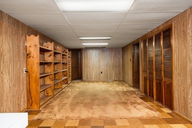 interior space featuring light carpet, wood walls, and a drop ceiling