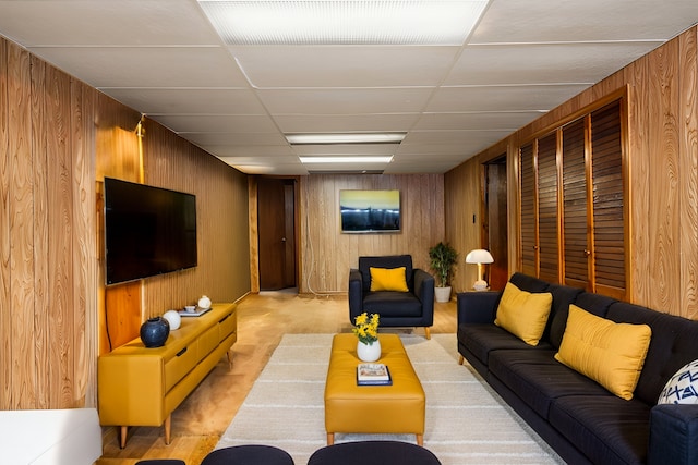 living area featuring a drop ceiling and wood walls