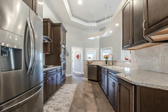 kitchen featuring light stone counters, a sink, dark brown cabinetry, stainless steel appliances, and a tray ceiling