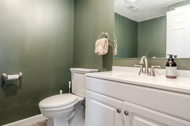 half bath featuring vanity, baseboards, visible vents, toilet, and a textured ceiling