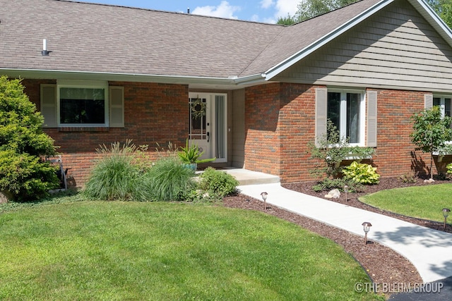 view of front of home with a shingled roof, a front yard, and brick siding