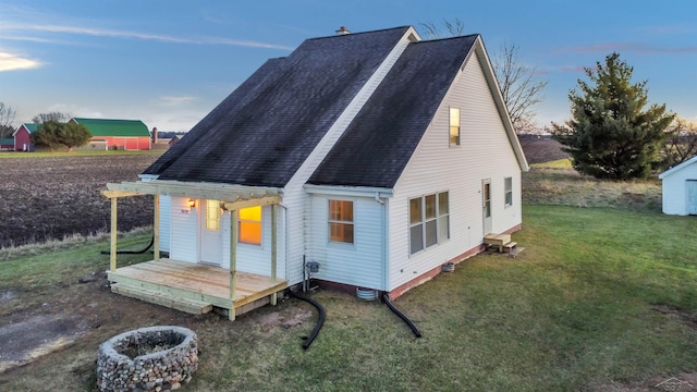 view of side of property with roof with shingles, a fire pit, and a yard