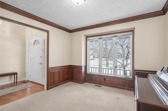 interior space featuring visible vents, crown molding, light colored carpet, wainscoting, and a textured ceiling