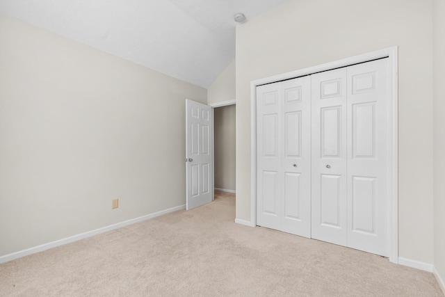 unfurnished bedroom featuring baseboards, light colored carpet, lofted ceiling, and a closet