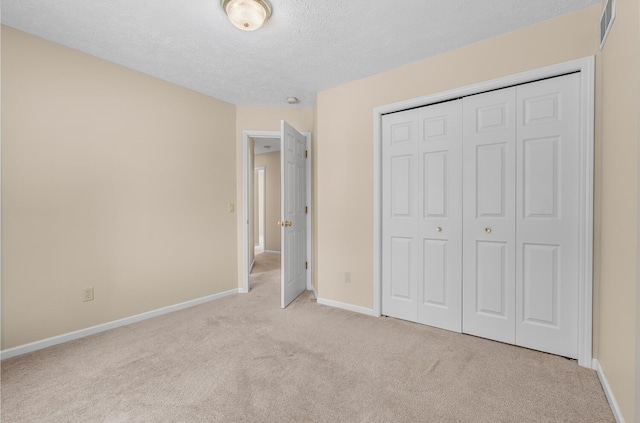 unfurnished bedroom featuring baseboards, visible vents, light carpet, a textured ceiling, and a closet